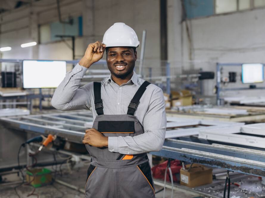 Smiling african american factory worker adjusting his hardhat in a window and door production line